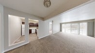 This single-floor residence offers a thoughtfully designed layout that balances open communal spaces with private retreats. The living area is generously sized, finished with warm neutral carpet and neutral-toned walls that create a bright, welcoming atmosphere. Large sliding glass doors flood the space with natural light and provide direct access to an outdoor patio, framing views of surrounding greenery.

The kitchen is efficiently arranged and features rich dark wood cabinetry paired with marble-style countertops for a polished contrast. White appliances including a refrigerator, electric range, over-the-range microwave, and dishwasher are all included. Light wood-look flooring ties the kitchen together and complements the overall neutral palette.

A secondary living or flex space offers additional room for a variety of uses, with carpet flooring and multiple doorways providing easy flow throughout the unit. The primary bedroom is spacious and includes direct access to a walk-in closet and an en suite bathroom. The bathroom features a dark-toned vanity with a white countertop, a large mirror, and a full soaking tub with a shower. Additional bathrooms mirror the same clean, modern aesthetic with updated fixtures and wood-look flooring throughout.