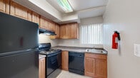 This single-floor residence offers a well-organized layout connecting living, sleeping, kitchen, and bathroom areas in a practical and comfortable arrangement. The kitchen is equipped with warm medium-toned wood cabinetry, dark granite-style countertops, and black appliances including an electric range, dishwasher, and refrigerator. A built-in range hood and a window with vertical blinds provide ventilation and natural light, while light tile flooring completes the clean, functional aesthetic.

The living and bedroom areas feature neutral-toned carpet throughout, creating a warm and cohesive feel. Windows dressed with vertical blinds allow ample natural light to filter in, with outdoor views of surrounding structures and mature trees. The rooms are finished with clean white baseboards and neutral wall tones, offering a versatile backdrop for a variety of interior styles.

A hallway connects the main living areas to the private rooms, with wood-look flooring transitioning into carpeted spaces. The bathroom features full beige tile wall surrounds with a decorative mosaic accent border, a soaking bathtub, and a window overlooking outdoor greenery, providing both privacy and natural light. Overall, the space presents a straightforward, functional design with consistent finishes throughout.