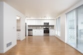 This well-designed single-floor unit offers a clean, contemporary aesthetic throughout. The open-concept living and dining area is bathed in natural light, courtesy of large sliding glass doors that lead to a private balcony and are complemented by floor-to-ceiling windows dressed with adjustable blinds. Warm hardwood-style flooring flows seamlessly across the entire unit, creating a cohesive and inviting atmosphere.

The kitchen is a standout feature, outfitted with crisp white cabinetry, a gray tile backsplash, neutral-toned countertops, and a full suite of stainless steel appliances including a range, microwave, and dishwasher. Ample upper and lower cabinet storage ensures generous functionality. A dedicated dining area adjacent to the kitchen benefits from its own set of large windows, filling the space with additional natural light and views of the surrounding neighborhood.

The living area is generously proportioned with smooth white walls and a ceiling fan, offering a versatile canvas for various furnishing arrangements. The bathroom is finished in a clean, minimalist style, featuring a full soaking tub with white subway tile surround, white cabinetry with dark hardware, and matching countertops consistent with the kitchen's design language. Overall, the unit presents a bright, modern, and move-in-ready living space.