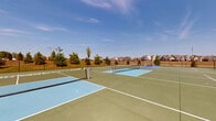 Located at 6650 Liberty Grand Blvd in Powell, Ohio, this outdoor recreational court complex offers a well-appointed multi-court facility designed for both pickleball and tennis enthusiasts. The complex features several courts finished in a combination of green and light blue surfaces, with crisp white boundary lines providing clear court demarcation. Each court is equipped with sturdy net posts and regulation nets, ready for competitive or recreational play.

The courts are fully enclosed by a black chain-link perimeter fence, ensuring safety and defining the play area. Overhead lighting poles are positioned throughout the facility, suggesting the ability to accommodate evening play. A waste receptacle is also available on-site for the convenience of players and visitors.

Surrounding the complex is a well-maintained landscape featuring young evergreen and deciduous trees, offering a pleasant natural backdrop. Views of the neighboring residential community are visible beyond the fencing, reflecting the facility's integration within a broader neighborhood setting. Adjacent green space and a nearby parking area enhance accessibility and usability for community members. The open-air design allows players to enjoy the outdoors under expansive Ohio skies, making this a vibrant and functional recreational amenity for the Powell community.