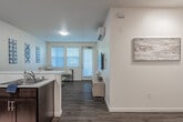 This single-floor unit offers a thoughtfully designed open-concept layout that seamlessly connects the kitchen, dining, and living areas. The kitchen is outfitted with rich dark-wood cabinetry, white countertops, and a full suite of stainless steel appliances, including a refrigerator, range, and microwave. Wood-look flooring flows throughout the main living spaces, adding warmth and continuity to the design.

The living room is bright and inviting, with multiple windows dressed in white blinds that allow generous natural light to fill the space. A wall-mounted television and a split-unit air conditioner serve the main area, enhancing comfort and functionality.

The unit includes multiple bedrooms, each carpeted and featuring large windows for natural light. One bedroom includes a spacious walk-in closet outfitted with dual hanging rods and built-in shelving, providing generous storage capacity.

Two full bathrooms are present in the unit. Each features dark-wood vanity cabinetry, white countertops with an undermount sink, a large mirror, and wood-look flooring. One bathroom includes a shower-tub combination, while the other offers a standalone vanity layout. Clean, neutral wall tones throughout the unit create a cohesive and versatile aesthetic well-suited to a variety of living arrangements.