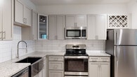 Located at 1500 Isner Ln in Garner, NC, this single-floor residence offers a thoughtfully designed layout with modern finishes throughout. The kitchen is a standout feature, showcasing gray shaker-style cabinetry, granite countertops, a classic white subway tile backsplash, and a full suite of stainless steel appliances including a range, over-the-range microwave, dishwasher, and refrigerator. A built-in wine rack and track lighting overhead add both function and style to the space. Light wood-tone flooring extends through the main living and kitchen areas, creating a warm, cohesive aesthetic. The bedroom is carpeted and benefits from natural light streaming through large windows fitted with horizontal blinds, complemented by a ceiling fan. A generously sized walk-in closet with extensive wire shelving provides ample storage. The bathroom features a tiled tub-shower combination with built-in corner shelving, a toilet, and overhead cabinetry for additional storage. Throughout the unit, neutral tones and clean lines establish a bright, contemporary ambiance, while the open sightlines from the main entry toward the kitchen create an inviting, connected feel.