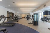 Located at 590 Downey Green St in Hampton, Virginia, this modern fitness center offers a comprehensive workout environment spread across a single level. The facility is divided into two distinct areas: a expansive main gym floor and a dedicated group exercise and cycling studio.

The main gym floor is generously proportioned, featuring durable dual-tone flooring with blue and tan zones that help define functional workout areas. It is outfitted with Matrix-brand cardio equipment including treadmills and ellipticals, a full complement of strength machines, a free weights station with a dumbbell rack, and weight benches. Floor-to-ceiling glass partitions and large windows along the perimeter flood the space with natural light and provide open views of the surrounding exterior. Overhead, modern linear pendant lighting and recessed fixtures ensure consistent illumination throughout.

The adjoining cycling and group exercise studio features light wood-look flooring, a row of Matrix and Keiser stationary bikes, stability balls, balance discs, and wall-mounted mirrors that expand the sense of space. A mounted flat-screen television provides entertainment or instruction during workouts.

Throughout both areas, the clean white walls, contemporary finishes, and well-organized layout create a bright, professional, and motivating atmosphere suited for a wide range of fitness activities.