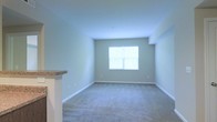 Located at 785 Cross Pointe Road in Gahanna, Ohio, this single-floor residence offers a clean, well-maintained living environment with a straightforward and functional layout. The living area is finished with plush wall-to-wall carpeting in a neutral gray tone, complementing the soft sage-green walls and crisp white baseboards that run throughout the space. A centered window allows natural light to fill the room, creating a bright and airy atmosphere. The ceiling is smooth and well-proportioned, contributing to an open and uncluttered feel. A partial wall or countertop element — finished with a granite-style surface — is visible at the edge of the living space, suggesting a seamless transition to a kitchen or bar area. The overall aesthetic is understated and move-in ready, with a palette of soft, neutral tones that provide a versatile backdrop for a variety of interior styles. The space presents a practical and comfortable single-level living option in the Gahanna area, with attention to clean finishes and a welcoming atmosphere throughout.