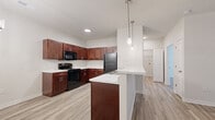 Located at 4131 Harmony Lane in Charlestown, Indiana, this single-floor, one-bedroom, one-bathroom unit offers a well-organized layout with consistent, modern finishes throughout. The open-concept kitchen and living area serves as the heart of the space, featuring rich dark-walnut shaker-style cabinetry, marble-look countertops, and black appliances including a range, microwave, and refrigerator. A peninsula with pendant lighting provides additional prep and seating space, while a dedicated dining nook with a chandelier adds definition to the area. Light wood-look luxury vinyl plank flooring runs throughout the main living spaces, contributing to a clean, cohesive aesthetic. The living room is bright and airy, benefiting from a ceiling fan and a sliding glass door with vertical blinds that allow natural light to fill the room. The bedroom offers comfortable carpeted flooring, neutral walls, and a closet, providing a cozy and functional retreat. The bathroom is well-appointed with a rich wood vanity, marble-look countertop, a large mirror with stylish vanity lighting, and a full tub-shower combination. A dedicated laundry area rounds out the unit's functional offerings, adding everyday convenience to this thoughtfully designed home.