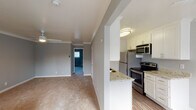 This single-floor residence offers a thoughtfully designed layout with a clean, neutral aesthetic throughout. The interior is painted in a consistent cool grey palette, complemented by white trim, crown molding, and crisp baseboards that lend a polished, cohesive feel to every room.

The kitchen stands out as a clear highlight, featuring a galley-style configuration with white shaker cabinetry, granite-look countertops, a double basin sink, and a full suite of stainless steel appliances including a refrigerator, electric range, and microwave. Wood-look flooring runs through the kitchen, adding warmth and durability to the space.

The living area is generously sized, finished with plush carpeting and accented by crown molding and a ceiling fan with light fixture. Multiple windows dressed with vertical blinds allow for natural light while maintaining privacy, and baseboard heaters provide consistent warmth. The space flows openly into adjoining areas, creating a connected and functional layout.

The bedrooms are carpeted and well-proportioned, each featuring windows with vertical blinds and baseboard heating. One bedroom includes a mirrored sliding-door closet, offering practical storage. The bathroom is finished with wood-look flooring, a sliding glass shower enclosure over a tub, and a bright window for natural ventilation.