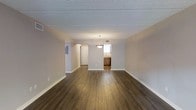 This upgraded 2-bedroom, 2-bathroom single-floor residence offers a well-designed layout that balances openness with defined living spaces. The interior is finished with rich, dark hardwood-style flooring that flows seamlessly throughout the main living and dining areas, creating a warm and cohesive aesthetic. Neutral light gray walls complement the flooring and contribute to a clean, contemporary feel.

The spacious main living area is bright and open, enhanced by large windows that invite natural light. A pendant light fixture serves as a focal point, adding a touch of understated elegance to the space. The layout connects the living area to the kitchen, which features warm wood cabinetry and functional counter space, making it ideal for everyday use.

The two bedrooms are well-proportioned and offer comfortable living quarters. The two full bathrooms are cleanly finished and conveniently positioned within the floor plan. Additional features include ample wall space, textured ceilings, and thoughtful storage solutions throughout.

Overall, this residence presents a practical yet polished living environment, with upgraded finishes that elevate the standard of comfort and style throughout every room.
