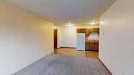 Located at 1153 Imperial Cir in Eau Claire, Wisconsin, this two-bedroom, one-bathroom unit offers a functional single-floor layout with a well-defined separation between living and sleeping spaces. The open kitchen and living area features warm honey-toned wood cabinetry, light countertops, and white appliances including a refrigerator and electric range. Durable wood-look flooring runs throughout the kitchen, while the living area transitions to plush wall-to-wall carpet. A sliding glass door in the living room opens to a balcony, bringing in natural light and outdoor access. Baseboard heating is present throughout, and a wall-mounted air conditioning unit serves the living area. Both bedrooms are carpeted and brightened by windows with neighborhood views. The primary bedroom is a comfortable size and features a double closet with built-in hanging rods, with direct access to the shared bathroom. The full bathroom includes a tub/shower combo and wood-look flooring complementing the warm wood-toned door frames and cabinetry found throughout the unit. Textured ceilings are consistent across all rooms, contributing to a cohesive, practical interior character suited for everyday living.