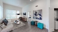 Located at 1105 E Katella Ave in Anaheim, California, this thoughtfully designed single-floor residence combines modern aesthetics with functional living spaces. The open-concept kitchen is a standout feature, showcasing dual-tone cabinetry with sleek gray upper cabinets and crisp white lower cabinets, stainless steel appliances, a white subway tile backsplash, and a central island with bar seating. A window above the sink frames a lush outdoor view, flooding the space with natural light. The living area impresses with soaring ceilings and multiple windows that invite abundant daylight, creating an airy and welcoming atmosphere. Curated wall art adds a contemporary artistic flair throughout. The bedrooms are serene and comfortable, each featuring large windows with garden views and plush carpeting. The primary bathroom offers a glass-enclosed walk-in shower, wood-look flooring, built-in open shelving, and a modern vanity. A secondary bathroom mirrors the clean design with a sleek vanity, large mirror, and a combination tub and shower. The entryway corridor is gallery-like, with carefully displayed artwork setting a refined tone from the moment you step inside. Overall, this residence exudes a cohesive modern style with warm, welcoming touches throughout.