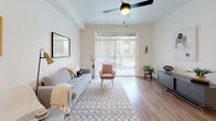 This single-floor residence showcases a cohesive modern design with warm wood-look flooring and crisp white walls throughout. The kitchen serves as a functional centerpiece, featuring dark wood-grain cabinetry, a white quartz peninsula with bar seating, stainless steel appliances including a gas range, microwave, refrigerator, and dishwasher, and pendant lighting that adds an industrial-chic touch. Recessed lighting and ample cabinetry make this space both practical and visually striking.

The living area is bright and welcoming, benefiting from natural light streaming through large sliding glass doors that open to an outdoor patio, offering views of lush greenery. A ceiling fan with a gold-toned fixture adds both style and comfort to the space.

Two bedrooms provide comfortable retreats, each featuring the same warm wood flooring and neutral walls. One bedroom benefits from a large window with horizontal blinds, allowing for natural light and outdoor views, while the other offers a quieter, more private atmosphere.

The bathroom maintains the unit's consistent design language, with a dark wood-grain vanity, white quartz countertop, a large mirror, and wood-look flooring, creating a clean and modern aesthetic throughout.