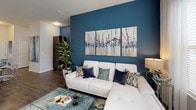 Located at 10051 Perimeter Station Dr in Charlotte, NC, this single-floor residence offers a well-designed layout that blends contemporary style with comfortable living. A cohesive blue color palette flows throughout the home, with bold accent walls anchoring each room and creating a vibrant yet unified aesthetic.

The living area is a standout space, featuring a deep teal feature wall adorned with a striking triptych artwork, hardwood-style flooring, and large windows dressed with sheer curtains and blinds that invite ample natural light. The open-concept kitchen is thoughtfully equipped with dark espresso cabinetry, granite-style countertops, a breakfast bar with pendant lighting, black appliances, and a tiled backsplash — ideal for both cooking and entertaining.

The primary bedroom offers a serene retreat with a soft blue accent wall, plush carpeting, and access to a private en-suite bathroom featuring a wide vanity, large mirror, and a walk-in closet. The second bedroom carries its own character with a bright teal accent wall, a four-poster bed frame, and generous natural light from large windows. A second full bathroom with a dark vanity and blue-toned walls serves this room and guests. Together, these spaces deliver a cohesive, modern living experience in a prime Charlotte location.