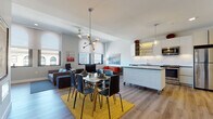 Located on S Main St in the heart of downtown Akron, Ohio, this single-floor unit offers a thoughtfully designed open-concept layout that seamlessly connects the living, dining, and kitchen areas. Light wood-tone flooring runs throughout the main living space, complementing the bright white walls and contemporary aesthetic.

The kitchen is outfitted with white flat-panel cabinetry, dark stone countertops, white subway tile backsplash, and a full suite of stainless steel appliances, including a range, microwave, dishwasher, and refrigerator. A rolling island provides additional prep space and doubles as a casual dining counter. A pendant light fixture adds a modern touch overhead.

The open dining area features a sizeable table beneath a sculptural sputnik chandelier, while the adjacent living room offers generous seating and tall arched windows framing panoramic views of Akron's downtown skyline and surrounding architecture. A second lounge area provides additional flexible seating.

The bedroom is carpeted and serene, with a large window offering city views, flanked by warm wood nightstands. The bathroom is finished with large-format tile flooring, a wall-mounted sink, backlit mirror, and a spacious glass-enclosed walk-in shower with marble-style tile surround and a rain showerhead.