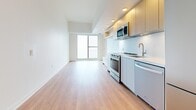 This well-appointed one-bedroom, two-bathroom unit in Toronto offers a thoughtfully designed layout that maximizes its compact footprint. Light-toned hardwood flooring flows seamlessly throughout the space, complementing the bright white walls and recessed lighting that create a clean, modern aesthetic.

The open-concept kitchen and living area forms the heart of the unit. The kitchen is outfitted with a full suite of stainless steel appliances, including a range, over-the-range microwave, dishwasher, and refrigerator. Light wood cabinetry paired with white lower cabinets and a white countertop lends a contemporary, two-tone look. A large window in the adjoining living area invites natural light, enhancing the airy feel of the space.

The unit includes two well-finished bathrooms. One features a floating wood-toned vanity, an illuminated mirror, and a bathtub, while the second offers a similar floating vanity with a walk-in glass-enclosed shower — both finished with neutral tile flooring and brushed nickel fixtures.

The bedroom is a cozy, functional space with access to a dedicated closet. Two hallways connect the rooms efficiently, contributing to a logical and comfortable flow. A dedicated closet provides additional storage. The overall design is modern and minimalist, suited for efficient urban living in Toronto.