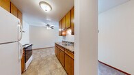 This single-floor unit offers a practical and well-organized layout designed for comfortable everyday living. The kitchen serves as a functional centerpiece, featuring warm honey-toned oak cabinetry with ample upper and lower storage, granite-look countertops, a double-basin sink, and a full suite of appliances including an electric range, refrigerator, and range hood. Tile flooring runs throughout the kitchen, providing a durable and easy-to-maintain surface. A ceiling fan overhead adds comfort to the adjacent dining or living area, which transitions seamlessly from the kitchen space.

The living area is generously proportioned, finished with soft carpeting and neutral walls that create a clean, versatile backdrop. A wall-mounted air conditioning unit and baseboard heating ensure year-round climate control. Natural light filters in through windows that frame views of the surrounding neighborhood.

The bedroom continues the carpeted flooring and offers a window with natural daylight, wood-trimmed details, and baseboard heating for added warmth. An entry area transitions between tiled and carpeted surfaces, offering a convenient threshold space.

The bathroom is neatly appointed with a single-vanity featuring a white countertop and mirrored medicine cabinet, classic mosaic tile flooring, and a full tub-shower combination with white tile surround. The overall aesthetic throughout the unit is clean, understated, and move-in ready.