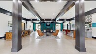 This single-story amenity center is designed to deliver a comprehensive lifestyle experience, combining recreation, fitness, and social spaces under one roof. The entrance lobby makes an immediate impression with soaring ceilings, bold teal accent walls, dark trim detailing, large multi-pane glass doors, and light-toned flooring that carries throughout the common areas. A crystal pendant chandelier anchors the entry, while generous natural light streams in through tall windows flanking the main doors.

The clubhouse lounge features exposed dark beam detailing, warm wood bar-height tables, upholstered seating, and pendant lighting, creating an inviting space for socializing or working. A quieter nook with a round table and velvet chairs offers a more intimate setting beside shuttered windows. A seating area near the entrance displays floor plans and greenery, lending a welcoming, informational quality.

The fitness center is thoroughly equipped with treadmills, an elliptical, rowing machine, adjustable bench, dumbbell rack, kettlebell station, cable machine, and medicine balls. Floor-to-ceiling mirrors, recessed lighting, and a checkerboard-patterned floor tile enhance the space visually and functionally.

A private screening room features tiered stadium-style seating with plush caramel-toned recliners set against deep teal walls. The exterior pool entrance features a covered porch with stone columns providing a graceful transition to the outdoor area.