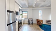 Located at 4748 N Kenmore Ave in Chicago's Uptown neighborhood, this single-floor unit showcases a modern industrial aesthetic defined by exposed structural beams, polished concrete floors, and a crisp white palette throughout. The open-concept living and kitchen area serves as the heart of the unit, where coffered ceilings with exposed ductwork lend a loft-like character. Multiple windows along the exterior walls invite natural light into the space while offering views of the surrounding neighborhood.

The kitchen is thoughtfully appointed with stainless steel appliances, including a full-size refrigerator, electric range, and built-in microwave. White flat-front cabinetry, a subway tile backsplash, and a single-basin sink complete the clean, functional design. The living area provides flexible space with room for casual dining and seating.

The bedroom is a quiet, well-defined room featuring a window that brings in natural light and exposed beam detailing consistent with the rest of the unit. An adjacent walk-in closet offers generous storage, outfitted with multiple hanging rods and shelving along three walls.

The bathroom maintains the minimalist aesthetic with polished concrete flooring, white walls, a toilet, and a walk-in shower. The entryway provides a practical transition into the unit with additional cabinetry nearby. Overall, the space delivers a cohesive industrial-modern atmosphere suited to urban living.