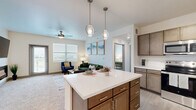 Located at 3234 W 31st St in Pueblo, Colorado, this single-story 2-bedroom, 2-bathroom residence offers a thoughtfully designed open-concept layout. The combined kitchen and living area serves as the heart of the home, anchored by a central island with sleek white quartz countertops, warm medium-toned cabinetry, stainless steel appliances, a double basin sink, and pendant lighting overhead. The kitchen flows seamlessly into the living room, which features plush carpeting, a ceiling fan, and a wall-mounted electric fireplace beneath a large flat-screen TV mount. Multiple windows and a private exterior door allow natural light to fill the space and provide outdoor access. The primary bedroom is a comfortable retreat with carpet flooring, a ceiling fan, and a direct en-suite bathroom connection, while the bathroom features an illuminated vanity mirror, wood-tone cabinetry, and quartz countertops. The second bedroom is equally well-lit, benefiting from a wide window and its own ceiling fan. Three generously sized closets, including a walk-in with wire shelving, provide ample storage throughout. A dedicated laundry area and a connecting hallway round out the functional floor plan, making this a complete and practical living space.