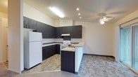 This single-floor space offers a well-designed, open-concept layout that seamlessly connects the kitchen and living area. The kitchen is a standout feature, showcasing dark espresso-toned cabinetry that extends from floor to ceiling, providing generous storage throughout. Light granite-style countertops offer a striking contrast against the rich cabinetry, while a peninsula extends into the space, creating an ideal spot for casual dining or meal prep. White appliances, including a refrigerator, electric range, and dishwasher, are neatly integrated into the layout. A range hood above the stove adds both function and a clean, finished look. Recessed lighting and a skylight-style fixture illuminate the kitchen with bright, even light. The adjoining living area is topped with a ceiling fan, promoting comfortable airflow throughout. Stone-patterned tile flooring runs through the kitchen and into the adjoining space, adding texture and durability underfoot. The neutral wall tones throughout create a calm, versatile backdrop that complements a variety of décor styles. Overall, the space strikes a practical balance between modern aesthetics and functional everyday living.