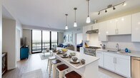 Located at 200 Albert Ave in East Lansing, MI, this thoughtfully designed one-bedroom, two-bathroom residence offers a contemporary open-concept layout across a single floor. The combined kitchen and living area serves as the heart of the home, anchored by a large center island with bar seating and elegant pendant lighting overhead. The kitchen is outfitted with white cabinetry, a stainless steel professional-grade range, a stainless steel refrigerator, a subway tile backsplash, and a vented range hood. Light wood-tone flooring flows seamlessly throughout the space. The living room opens to a private balcony through expansive floor-to-ceiling sliding glass doors, offering sweeping outdoor views and exceptional natural light. The well-proportioned bedroom features a large window framing treetop views, creating a calm and comfortable retreat. Two closets with built-in wire shelving systems provide generous storage. Both bathrooms are finished with white vanities, white quartz countertops, large framed mirrors, and wood-look flooring; the primary bath includes a dual-sink vanity and a glass-enclosed shower with tile surround. A connecting hallway ties the layout together efficiently, completing this polished and functional residence.