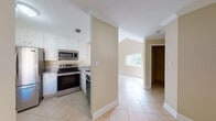 Located at 800 The Pointe Dr in West Palm Beach, Florida, this single-floor residence offers a bright and open layout designed for comfortable living. Light-toned tile flooring runs consistently throughout the home, complementing the warm beige walls and crisp white trim and crown molding found in every room.

The spacious living area is a standout feature, boasting soaring vaulted ceilings that lend an airy, open feel to the space. Large sliding glass doors and additional windows flood the room with natural light and provide direct access to an outdoor area, offering views of the surrounding greenery. A pass-through window connects the living area to the kitchen, enhancing the open-concept flow.

The kitchen is well-appointed with white cabinetry, marble-look countertops, and a full suite of stainless steel appliances, including a refrigerator, range, over-the-range microwave, and dishwasher. A window above the sink brings in additional natural light.

The bedroom features crown molding, a large window with outdoor views, and access to a walk-in closet. The bathroom is finished with floor-to-ceiling tile wainscoting, a marble-top vanity with a framed mirror, and a textured upper wall treatment, giving it a clean and polished appearance. A walk-in closet is conveniently located adjacent to the bathroom.