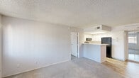 Located at 3535 West Tierra Buena Lane in Phoenix, Arizona, this two-bedroom, one-bathroom residence offers a functional and efficient single-floor layout. The open living area flows seamlessly into the kitchen, which features white cabinetry, a skylight panel for added brightness, wood-look vinyl flooring, and black appliances including a refrigerator, range, and over-the-range microwave. A breakfast bar peninsula separates the kitchen from the carpeted living space, creating a natural division while maintaining an open feel. Neutral tones and textured ceilings carry throughout the unit, giving the space a clean, uniform appearance. Both bedrooms are carpeted and filled with natural light through barred windows, each equipped with sliding closet doors for convenient storage. The primary bedroom includes sliding glass door access to an outdoor area. The bathroom is well-appointed with a white vanity featuring stone-look countertops, wood-look flooring, grab bars, and a combined tub and shower. The overall design is straightforward and functional, offering a comfortable living environment suited for everyday use in the Phoenix metro area.