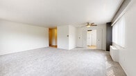 This single-floor residence offers a practical and comfortable layout with a clean, neutral aesthetic throughout. The spacious living area is finished with plush light-gray carpeting and includes a ceiling fan with a built-in light, creating a bright and airy atmosphere. The room opens conveniently toward the kitchen, making it well-suited for everyday living.

The galley-style kitchen is efficiently designed with white cabinetry, granite countertops, hardwood-style flooring, and white appliances including a range and refrigerator. Ample upper and lower cabinet storage lines both sides of the kitchen, maximizing functionality in the space.

A hallway with hardwood-style flooring and a gold-toned flush ceiling fixture connects the main living areas to the private quarters. The generously sized bedroom features soft carpeting, a ceiling fan, and a large window dressed with vertical blinds that allows natural light to fill the room. A walk-in closet provides excellent storage, and direct access to a full bathroom adds a convenient ensuite-like setup.

Two full bathrooms serve the residence. One includes a tub-shower combination with white tile surround, a white vanity with under-sink cabinetry, a large mirrored medicine cabinet, and hardwood-style flooring. The second bathroom mirrors this design with the addition of a glass-enclosed stand-up shower.