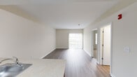 This single-floor residence offers a bright, open-concept layout designed for comfortable everyday living. The living area is finished with warm wood-tone laminate flooring and neutral beige walls, creating a clean and inviting atmosphere. A sliding glass door with vertical blinds allows abundant natural light to fill the space while providing access to an outdoor balcony area with exterior views.

The kitchen is thoughtfully appointed with rich cherry-toned cabinetry, light countertops, and a full suite of black appliances including a refrigerator, range, and oven. A peninsula with an integrated sink and additional counter space separates the kitchen from the living area, offering both functionality and an open feel ideal for entertaining or daily use.

The bedrooms feature plush carpeting and neutral wall tones, with windows fitted with horizontal blinds that allow for adjustable natural light. Each bedroom includes closet access, providing practical storage solutions.

The full bathroom is finished with wood-toned cabinetry, a white countertop vanity, and a full tub-shower combination. Light laminate flooring and clean white fixtures contribute to a bright, functional space.

Throughout the residence, consistent neutral tones, clean lines, and a cohesive design palette create a calm and versatile environment ready to accommodate a variety of personal styles.
