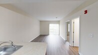 This single-floor residence offers a bright, open-concept layout designed for comfortable everyday living. The living area is finished with warm wood-tone laminate flooring and neutral beige walls, creating a clean and inviting atmosphere. A sliding glass door with vertical blinds allows abundant natural light to fill the space while providing access to an outdoor balcony area with exterior views.

The kitchen is thoughtfully appointed with rich cherry-toned cabinetry, light countertops, and a full suite of black appliances including a refrigerator, range, and oven. A peninsula with an integrated sink and additional counter space separates the kitchen from the living area, offering both functionality and an open feel ideal for entertaining or daily use.

The bedrooms feature plush carpeting and neutral wall tones, with windows fitted with horizontal blinds that allow for adjustable natural light. Each bedroom includes closet access, providing practical storage solutions.

The full bathroom is finished with wood-toned cabinetry, a white countertop vanity, and a full tub-shower combination. Light laminate flooring and clean white fixtures contribute to a bright, functional space.

Throughout the residence, consistent neutral tones, clean lines, and a cohesive design palette create a calm and versatile environment ready to accommodate a variety of personal styles.