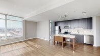 Located at 2827 Telek Pl in Alexandria, VA, this modern two-bedroom, two-bathroom residence offers a thoughtfully designed open-concept layout with clean contemporary finishes throughout. The combined kitchen and living area serves as the heart of the home, featuring light wood-tone flooring, a central island with a white quartz countertop, and a sleek kitchen outfitted with dark wood cabinetry, a tile backsplash, and a full suite of stainless steel appliances. Floor-to-ceiling windows in the living area flood the space with natural light and frame expansive views of the Alexandria cityscape. Both bedrooms are carpeted for comfort, with the primary bedroom benefiting from a generous footprint and large windows offering wide panoramic views. Each bedroom is paired with its own bathroom, both finished with light tile flooring, modern dark-toned vanities, and white countertops. A dedicated closet with built-in shelving and hanging rods provides ample storage. Neutral, warm-toned walls and crisp white trim carry a cohesive aesthetic throughout, lending the residence a bright and welcoming ambiance well-suited to contemporary urban living.