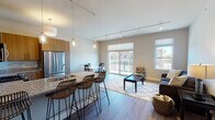This thoughtfully designed single-floor residence offers a seamless open-concept layout that connects the kitchen, dining, and living areas into one cohesive and functional space. The kitchen is a standout feature, equipped with stainless steel appliances including a gas range, over-the-range microwave, and a full-size refrigerator. Warm wood cabinetry, granite countertops, a glass tile backsplash, and a built-in wine cooler complete the space. A breakfast bar with rattan barstools provides additional seating and connects the kitchen to the dining area. The living room is bright and welcoming, featuring track lighting, hardwood-style flooring, and multiple windows that flood the space with natural light. A sliding glass door opens to a private balcony with views of the surrounding neighborhood. The bedroom is a serene retreat with plush carpeting, a ceiling fan, and a walk-in closet. A high clerestory window adds an architectural touch while allowing additional natural light. The bathroom is finished with granite countertops, wood cabinetry, tile flooring, and a glass-enclosed walk-in shower with full tile surround. Neutral tones and modern finishes throughout create a clean, contemporary ambiance.