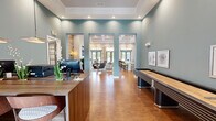 Located at 30 Gates Mill St in Huntsville, Alabama, this single-floor community clubhouse offers a well-appointed gathering space designed with modern sophistication. The interior is anchored by warm hardwood-style flooring and a cohesive teal and white color palette that flows throughout.

The reception area greets visitors with a handsome wood-finished front desk, complemented by recessed lighting and a tray ceiling detail overhead. Adjacent to the reception, a full-size shuffleboard table adds a recreational focal point, while framed artwork decorates the walls.

The lounge area is a standout, featuring soaring coffered ceilings, recessed lighting, and large French doors that invite abundant natural light and outdoor views of the pool area. A dramatic accent wall clad in reclaimed wood planks anchors a sleek, built-in electric fireplace with a mounted flat-screen television above. Comfortable seating, tall tropical plants, and layered area rugs complete the inviting atmosphere.

A wet bar and kitchen counter with bar seating serves as an entertainment hub, finished with a textured stone backsplash, dark cabinetry, and pendant lighting above.

A dedicated business center provides two computer workstations beneath soaring teal walls and pendant lights, offering a quiet and functional workspace within the clubhouse.