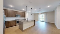 This well-appointed single-floor residence showcases a thoughtfully designed open-concept layout that seamlessly connects the kitchen, dining, and living areas. The contemporary kitchen is a standout feature, equipped with rich wood-toned cabinetry extending to the ceiling, quartz countertops, stainless steel appliances including a French door refrigerator and range, and a large center island with a matte black faucet. Stylish globe pendant lights hang above the island, adding a modern touch. Light wood-tone flooring flows throughout the main living areas, enhancing the bright and airy ambiance. The living area is fitted with a ceiling fan and opens directly to a private balcony through sliding glass doors, allowing for generous natural light and outdoor views. The bedrooms feature plush carpeting, ceiling fans, and oversized windows that frame pleasant outdoor scenery. The primary suite includes a spacious walk-in closet with wrap-around hanging rods and a well-designed en-suite bathroom offering both a soaking tub and a glass-enclosed shower with large-format tile surround and matte black hardware. A dedicated in-unit laundry room with a full-size washer and dryer completes this functional and contemporary living space.