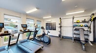 Located in Tigard, Oregon, this fitness center is a compact yet comprehensively outfitted space designed to support a full range of workout routines. The single-room layout is efficiently organized to maximize functionality, with durable rubber flooring throughout that provides both safety and comfort during exercise.

The cardio zone features treadmills, an elliptical trainer, and a stationary spin bike, several of which are equipped with integrated display screens. Large windows along multiple walls allow ample natural light to fill the space and provide views of the surrounding outdoor environment, contributing to an energizing atmosphere.

The strength training area is anchored by a multi-functional squat and power rack with TRX suspension straps, accompanied by a tiered storage rack stocked with medicine balls, kettlebells, and weight plates. An adjustable workout bench completes the free weights section. A wall-mounted mirror expands the visual depth of the room and supports proper form during training.

Climate control is handled by a wall-mounted mini-split unit, ensuring year-round comfort. Motivational signage — featuring phrases such as "Believe," "Focus," and "Discipline" — adorns the walls alongside a bold typographic mural, reinforcing the space's purpose-driven design. A glass-partitioned door at one end offers a glimpse into an adjacent room, suggesting additional amenity access nearby.