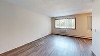 Located at 1721 Marion St in Roseville, MN, this one-bedroom apartment offers a practical and comfortable layout across a single floor. The combined kitchen and living area forms the heart of the unit, with the living room featuring durable hardwood-style flooring, a textured ceiling, a wall-mounted air conditioning unit, and a large window with vertical blinds that fills the space with natural light and outdoor views of surrounding greenery. The galley-style kitchen is equipped with rich, dark wood cabinetry, light countertops, a double-basin sink, a white electric range, and a refrigerator — all flowing efficiently within the space. The generously sized primary bedroom is finished with plush carpeting, a ceiling fan with light fixture, and two windows that bring in additional natural light. It features direct access to a dedicated closet with built-in shelving and sliding wood-panel doors, offering ample storage. A secondary entry area with hardwood-style flooring and a built-in closet provides additional organization space. Baseboard heating is present throughout, ensuring year-round comfort. Warm wood-toned door and window trim accents tie the interior together, giving the unit a cohesive, residential feel.