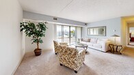 Located at 1200 Vineyard Dr in Broadview Heights, Ohio, this well-appointed 2-bedroom, 2-bathroom residence offers a comfortable and functional single-floor layout. The spacious living room is a true highlight, featuring soft carpeting, light gray walls, and expansive floor-to-ceiling sliding glass doors that open to a private balcony, flooding the space with natural light and offering pleasant outdoor views of the surrounding landscape. The kitchen is efficiently designed with white cabinetry, granite-style countertops, marble-look tile flooring, and a full suite of white appliances, providing ample storage and workspace. The generously sized primary bedroom benefits from large windows dressed with vertical blinds, allowing soft, diffused light to fill the carpeted space. The second bedroom features bright white walls accented with decorative gold polka-dot details and a large window that brings in abundant natural light, making it a versatile room. Both bathrooms are finished with marble-look tile flooring and white fixtures — one offering a full tub-shower combination with classic white subway tile surround, and the other featuring a white vanity with medicine cabinet. The overall ambiance of the residence is clean, bright, and welcoming throughout.