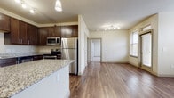 This single-floor residence offers a thoughtfully designed open-concept layout that seamlessly connects the kitchen, dining, and living areas. The kitchen is a standout feature, equipped with rich dark-brown cabinetry, granite countertops, and a full suite of stainless steel appliances including a refrigerator, electric range with microwave, and dishwasher. A peninsula with a granite countertop provides additional prep space and serves as a natural divider between the kitchen and the main living area. Warm hardwood-style flooring flows throughout the main living spaces, complemented by neutral-toned walls that create a bright and welcoming ambiance. The living area benefits from a ceiling fan and multiple windows fitted with blinds, allowing for ample natural light and ventilation. A dedicated in-unit laundry area accommodates a front-load washer or dryer, adding everyday convenience. The bedroom features its own ceiling fan and direct access to a generous walk-in closet with built-in shelving and carpeted flooring. The bathroom is finished with tile-surround tub and shower combination and hardwood-style flooring, offering a clean and functional design throughout.