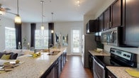 This well-designed single-floor residence offers a thoughtful layout that balances style and functionality. The heart of the home is a spacious, open-concept kitchen featuring rich dark cabinetry, light granite countertops, and a full suite of stainless steel appliances including a range, microwave, dishwasher, and refrigerator. A generous kitchen island with a double sink serves as a natural focal point and gathering space, illuminated by elegant pendant lighting. Wood-style flooring flows throughout the main living areas, adding warmth and continuity.

The living room is bright and inviting, benefiting from large windows and a glass door that invite natural light and provide views of the outdoors. The neutral color palette and clean lines create a calm, contemporary ambiance throughout.

Two well-proportioned bedrooms are finished with plush carpet and feature large windows dressed with sheer curtains and blinds, allowing for abundant natural light. The primary bedroom includes a walk-in closet and direct access to an en-suite bathroom with a glass-enclosed shower and tile flooring. A second bathroom features hardwood-style flooring and a dark-cabinet vanity with a white countertop, maintaining the cohesive design aesthetic found throughout the residence.