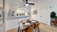 This well-appointed single-floor residence offers a thoughtfully designed layout that balances comfort and modern style throughout. A welcoming entry hallway, adorned with framed artwork, leads directly into the bright and open living area. The living room is a standout space, featuring light wood flooring, a bold navy accent wall, and a full-width sliding glass door that opens onto a private balcony, flooding the room with natural light and providing pleasant outdoor views.

Adjacent to the living area, the dining space is defined by a ceiling fan overhead and a half-wall pass-through that connects seamlessly to the galley kitchen. The kitchen is well-equipped with two-tone cabinetry — navy lower cabinets paired with crisp white uppers — complemented by white quartz countertops, a geometric tile backsplash, stainless steel appliances, and a black matte faucet.

The residence includes two comfortable bedrooms, each with windows that bring in natural light and offer a calm, restful atmosphere. Both rooms feature wood-style flooring and neutral walls that lend a clean, versatile aesthetic. The full bathroom is finished with white tile, a combination tub and shower, and a navy vanity that ties into the home's consistent design palette throughout.