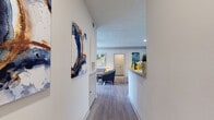 This single-story residence offers a thoughtfully designed layout that flows naturally from the entry through each living space. A welcoming hallway, decorated with colorful abstract artwork, leads into the open-concept living and dining area. The living room features light wood-style flooring, a ceiling fan, and ample wall space showcasing large-scale artwork, while the adjacent dining area accommodates a round glass table with seating for four. Both spaces benefit from recessed lighting and a neutral color palette that enhances the sense of openness.

The galley-style kitchen runs along one wall and is equipped with gray cabinetry, light countertops, a stainless steel sink, and stainless steel appliances. A peninsula provides additional counter space and separates the kitchen from the living area.

The residence includes multiple bedrooms, each carpeted and featuring windows with blinds and curtain rods that allow for natural light and privacy. Ceiling fans are present in select bedrooms. Two full bathrooms serve the residence, each featuring wood-style flooring, a vanity with a large mirror, ample cabinet storage, and a shower-tub combination. The overall ambiance is clean, contemporary, and move-in ready.