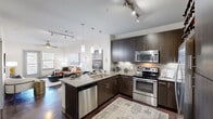 Located at 600 Fort Worth Ave in Dallas, Texas, this single-floor residence showcases a thoughtfully designed open-concept layout with modern finishes throughout. The kitchen is a standout feature, boasting dark espresso cabinetry, granite countertops, a central island with bar seating, stainless steel appliances including a built-in microwave and electric range, a subway tile backsplash with under-cabinet lighting, and elegant pendant lighting above the island. Track lighting overhead adds further illumination, while the space flows seamlessly into the living area. The living room offers polished concrete floors, a ceiling fan, and natural light through a glass door and windows. A secondary sitting area provides additional flexible living space with natural light and dark hardwood-style flooring. Both bedrooms feature plush carpeting, ceiling fans, and windows that bring in natural light. The bathroom includes a soaking tub with large-format dark tile surround, granite vanity countertops, and direct access to a walk-in closet with built-in shelving. A dedicated laundry area houses a full-size washer and dryer, flanked by dark cabinetry for additional storage. The overall ambiance is contemporary and cohesive, combining functional design with upscale residential finishes.