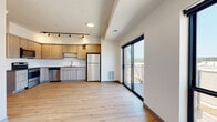 This contemporary single-floor residence offers a thoughtfully designed open-concept layout that seamlessly connects the kitchen and living areas. The kitchen is a standout feature, equipped with light wood cabinetry, a subway tile backsplash, stainless steel appliances including a refrigerator, range, microwave, and dishwasher, along with ample counter space. Track lighting overhead adds a modern, functional touch to the space.

Light wood-tone flooring runs throughout the unit, lending warmth and visual continuity across every room. The living area is bright and airy, benefiting from large windows that invite natural light and offer views of the surrounding cityscape. A full-width sliding glass door opens directly onto a private balcony, extending the living space outdoors with scenic views beyond.

The bedroom is generously proportioned, featuring large windows that continue the theme of natural light and outdoor connectivity. A spacious walk-in closet with multi-level wire shelving provides excellent storage and organization potential.

The bathroom is clean and well-appointed, featuring a combination soaking tub and shower with a curved curtain rod, chrome fixtures, and the same light wood flooring found throughout the unit. The overall aesthetic is modern and minimalist, with crisp white walls and clean lines creating a fresh, move-in-ready ambiance.