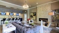 Located at 471 N Hamilton Rd in Gahanna, Ohio, this single-floor space combines upscale design with a warm, welcoming ambiance. The main lounge area immediately draws attention with a striking crystal chandelier that anchors the room and casts a refined glow over the space. A floor-to-ceiling stacked stone accent wall frames a sleek, linear gas fireplace, creating a dramatic focal point that adds both warmth and texture to the interior. Neutral, earthy wall tones complement the polished concrete flooring, lending the space a modern yet inviting character. The seating area is furnished with a generously sized tufted sectional sofa and a glass-top coffee table, offering a comfortable and stylish gathering space. Bold contemporary artwork adorns the walls, adding a curated, gallery-like feel throughout. Crown molding and recessed lighting contribute refined architectural details. Adjacent to the lounge, a well-appointed bar area features dark cabinetry, bar seating, and a mounted television, making it ideal for social gatherings or events. Natural light filters in through exterior-facing doors, brightening the interior. Overall, the space presents a polished, sophisticated atmosphere suited for entertaining and community engagement.