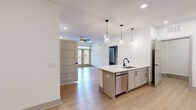 Located in Candler, NC, this single-story 2-bedroom, 2-bathroom home offers a clean, modern aesthetic with warm light wood-tone flooring and crisp white walls throughout. The open-concept kitchen is a standout feature, boasting gray shaker-style cabinetry, white subway tile backsplash, stainless steel appliances including a French door refrigerator and range, and a large peninsula with quartz countertops illuminated by a trio of glass pendant lights — ideal for both cooking and casual dining. The living area is bright and airy, featuring recessed lighting, a ceiling fan, and glass doors that invite natural light and outdoor access, alongside a built-in closet nook. The primary bedroom is generously sized with natural light from a large window and a ceiling fan overhead. The second bedroom offers similar comfort with natural light and a clean, open layout. Both bathrooms are thoughtfully finished with gray shaker vanities, black hardware accents, and large framed mirrors. One bathroom features a tub-shower combo, while the other is designed with accessibility in mind, featuring grab bars and an open layout. A dedicated laundry room with a full-size washer and dryer adds everyday convenience. The hallway connects all spaces with a tidy, well-lit flow, completing this carefully designed home.