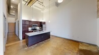 Located at 1101 Hawthorne Lane in Charlotte's vibrant Plaza Midwood neighborhood, this 1-bedroom, 1-bathroom loft showcases an industrial-chic aesthetic with dramatic soaring ceilings and polished concrete floors throughout. The open-concept living and kitchen area is anchored by a large island with granite countertops, dark wood cabinetry, and stainless steel appliances, all illuminated by stylish pendant lighting. A striking exposed brick wall with floor-to-ceiling black-framed windows floods the space with natural light. The bedroom includes a closet with in-unit washer/dryer hookups. The bathroom features tile flooring, a granite vanity, and a full tub/shower combo.