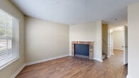 Located in Chattanooga, TN, this two-story residence offers a well-organized layout across two levels. The living area is a welcoming, open space highlighted by rich wood-look flooring and a classic brick fireplace with a tiled hearth, serving as a natural focal point. A staircase connects the two floors, adding a sense of vertical space to the home's overall design. The textured ceilings and neutral warm-toned walls throughout create a consistent, comfortable ambiance.

The kitchen is a standout feature, outfitted with dark shaker-style cabinetry, granite-look countertops, and a striking mosaic tile backsplash in earthy tones of brown, gray, and cream. Black appliances — including a range, dishwasher, and refrigerator — complement the cabinetry for a cohesive, modern aesthetic. The same wood-look flooring continues seamlessly from the main living areas into the kitchen.

Additional spaces include a dedicated room with wood-look flooring and a built-in HVAC vent, suitable for a bedroom or office, as well as a spacious walk-in closet with wire shelving for ample storage. The bathroom features a full-size soaking tub with a clean white surround. The home's layout, as seen from the dollhouse view, reveals a compact and efficiently designed floor plan ideal for comfortable day-to-day living.