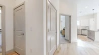 This well-appointed single-floor residence showcases a clean, contemporary design with a cohesive neutral palette carried throughout every room. Light hardwood flooring flows through the main living areas and hallways, complemented by crisp white walls and panel-style interior doors with brushed gold hardware that lend a modern, refined touch.

The living room is a bright, welcoming space anchored by large windows that flood the room with natural light and offer views of the surrounding neighborhood. Vaulted ceilings add to the sense of openness, while recessed lighting provides additional illumination. The kitchen is thoughtfully designed with white cabinetry, granite countertops, a subway tile backsplash, and a full suite of stainless steel appliances. A central island with bar seating makes it ideal for both cooking and casual dining.

The bedrooms offer comfortable retreats, each featuring plush carpeting, generous wall space, and windows that invite natural light. The primary bedroom is particularly spacious, with room for a full furniture arrangement. The bathroom is finished with granite-topped white vanity cabinetry, hardwood-style flooring, and a tiled tub-shower combination, balancing practicality with style.

A well-organized hallway connects the rooms seamlessly, reflecting a thoughtful, functional floor plan designed for comfortable everyday living.