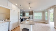 Located at 3221 Glenhill Dr in Raleigh, NC, this well-appointed 2-bedroom, 2-bathroom single-floor home offers a thoughtfully designed open-concept layout with modern finishes throughout. The kitchen serves as the centerpiece of the main living area, featuring gray cabinetry, granite countertops, stainless steel appliances, and a central island with a built-in sink and pendant lighting overhead. Light hardwood flooring flows seamlessly through the kitchen and living areas, creating a warm and cohesive aesthetic. Large windows throughout the home invite abundant natural light and offer pleasant views of the surrounding greenery. An in-unit laundry area is conveniently integrated into the main living space. Both bedrooms are carpeted and generously sized, with the primary bedroom offering comfortable dimensions and access to a well-appointed en-suite bathroom. The primary bath features a granite vanity with gray cabinetry, a glass-enclosed walk-in marble tile shower, and direct access to a walk-in closet with built-in wire shelving. The second bathroom mirrors the same refined finishes with a granite vanity and hardwood-style flooring. Each bedroom is served by its own closet, providing ample storage throughout.