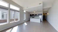 This 2-bedroom, 2-bathroom residence offers a thoughtfully designed open-concept floor plan that seamlessly connects the living and kitchen areas. The space is filled with natural light streaming through large windows, highlighting the clean lines and modern finishes throughout. Soaring ceilings amplify the sense of spaciousness in the main living area, which features smooth light-toned hardwood-style flooring that extends throughout the unit.

The kitchen is a standout feature, showcasing dark cabinetry paired with a crisp white island that provides both additional counter space and casual seating. Stainless steel appliances, including a refrigerator and microwave, complement the sleek tile backsplash, while pendant lighting adds a warm, contemporary touch overhead. The open layout allows the kitchen to flow naturally into the living area, making it ideal for entertaining.

The neutral color palette of soft whites and grays lends a clean, modern aesthetic throughout the space. The high ceilings and generous window placement ensure the unit remains bright and airy. The single-floor layout provides a convenient and cohesive living experience, with each area transitioning smoothly into the next, creating a functional and stylish home.