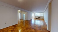 This single-floor residence is defined by its classic parquet wood flooring, which runs throughout the living spaces and bedrooms, lending a warm, timeless character to the interior. The open living and dining area is generously proportioned, with white walls, a smooth ceiling, and large windows that allow natural light to fill the space. A wall-mounted air conditioning unit and baseboard heating ensure year-round comfort.

The kitchen is efficiently arranged, featuring warm wood cabinetry, a white gas range with overhead ventilation, and a white refrigerator, providing practical functionality for daily use.

Two bedrooms offer quiet, well-sized retreats, each continuing the parquet flooring and featuring built-in closets with ample storage. Recessed lighting adds a clean, modern touch to these rooms.

The unit includes two bathrooms. One features a glass-enclosed shower stall, a white vanity with a light marble-toned countertop, and full white tile surrounds. The second bathroom includes a bathtub, matching white tile walls, a toilet, and a mirrored medicine cabinet above the vanity. Both bathrooms maintain a clean, utilitarian aesthetic consistent with the overall design of the space.