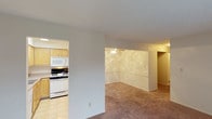 This single-floor unit is designed with a straightforward, functional layout that connects the main living areas efficiently. The living room is a generously sized space finished with neutral-toned wall-to-wall carpeting and features a sliding glass door with vertical blinds that allows natural light to filter in and provides access to an outdoor area. A ceiling fan overhead and baseboard heating units along the walls ensure year-round comfort, while a wall-mounted air conditioning unit adds additional climate control.

The kitchen is separated from the living area and is well-equipped with light wood cabinetry that extends to the upper walls, offering ample storage. Countertops provide considerable workspace, and the kitchen includes a gas range with oven, a built-in microwave, a dishwasher, a refrigerator, and a double-basin sink. Light tile flooring completes the practical, easy-to-maintain space.

The bedrooms are carpeted and feature textured ceilings, baseboard heaters, and windows that bring in natural light. Each room offers a calm, neutral palette suited for comfortable living. Closet access is available within the bedroom area, supported by a wood-paneled door.

The bathroom includes a full-sized soaking tub with a shower surround, a toilet, and a vanity, all finished in clean white tones for a bright, functional feel.